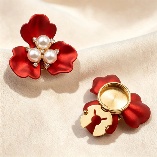 Vibrant satin red three-petal floral button cover centered with three white pearls and sparkling rhinestones. The right piece highlights the open gold attachment clip for effortless French-style cuff styling under warm sunlight.