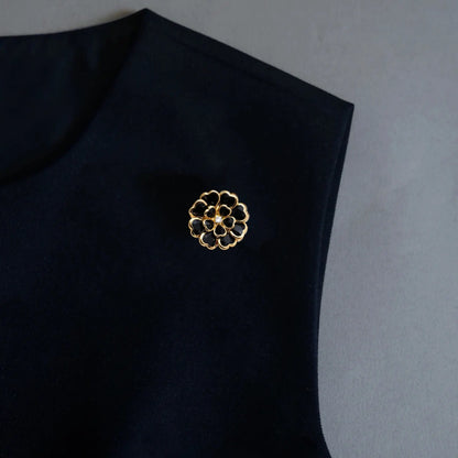 A sophisticated black-on-black styling image showcasing a 2-in-1 black enamel floral accessory utilized as a brooch pin. The intricate gold outlines and crystal center stand out beautifully against the dark fabric, perfectly embodying an old money aesthetic.