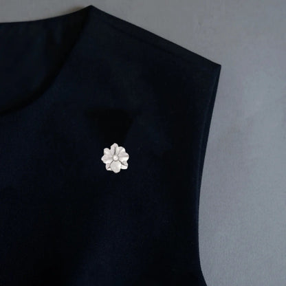 A sleek minimalist styling shot featuring a 2-in-1 brushed silver floral accessory, worn as an elegant brooch pin on a black garment. With its textured petals and central pearl, this piece offers a cool, contemporary light luxury accent for modern outfits.