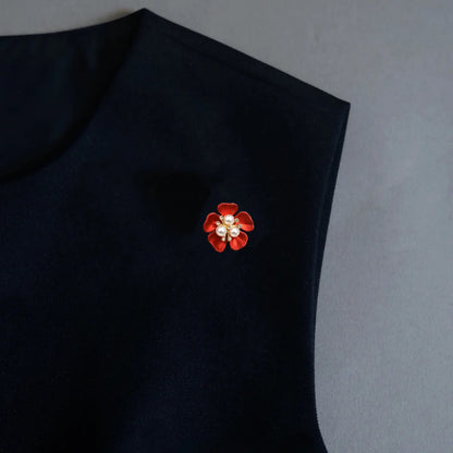 A striking styling photo showcasing a 2-in-1 classic red enamel floral accessory utilized as a statement brooch pin on a black sleeveless top. Featuring a central pearl design, this vibrant piece instantly elevates minimalist wardrobes with a sophisticated pop of color.