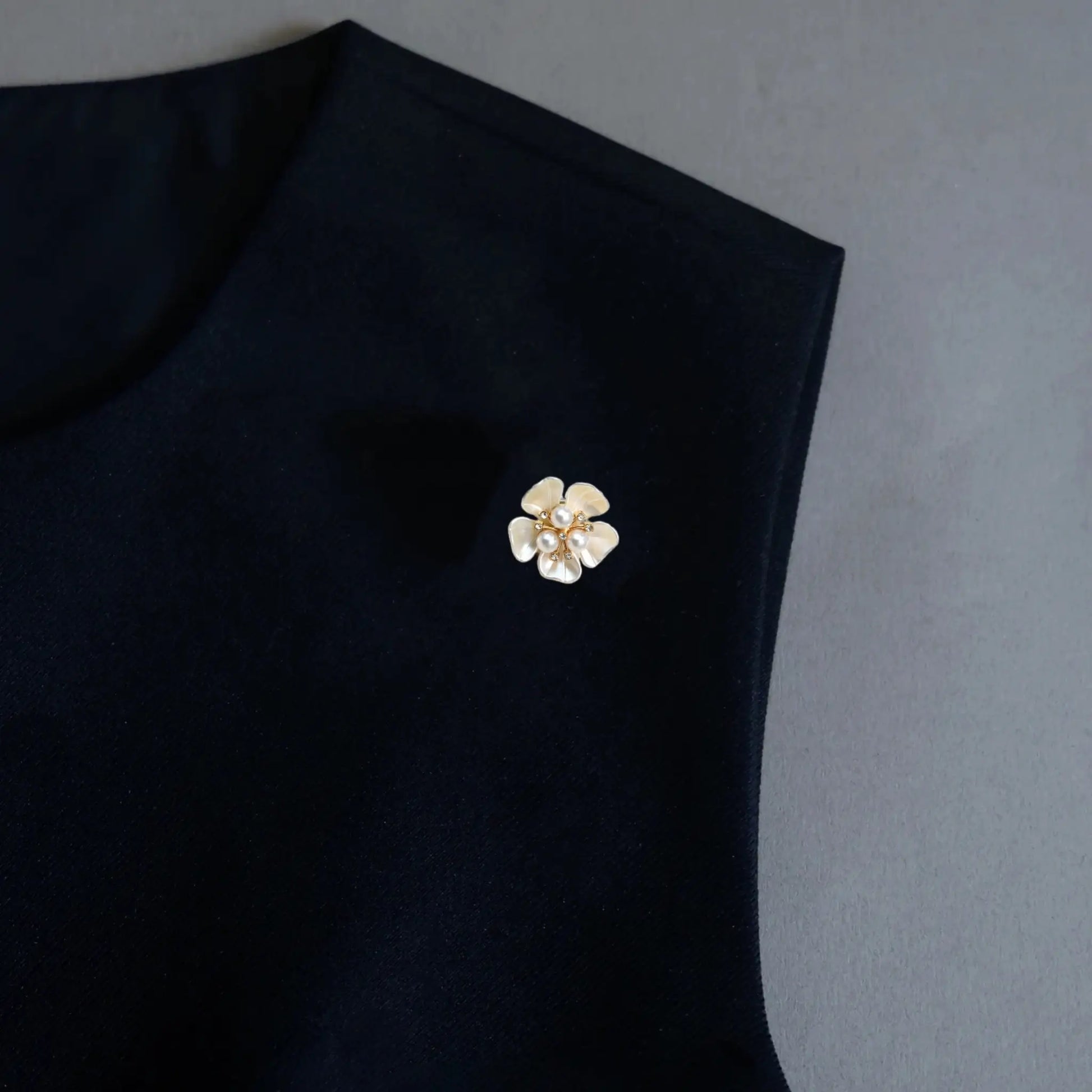 A refined minimalist shot demonstrating the 2-in-1 functionality of a creamy white enamel floral accessory, styled as a chic lapel pin on a black dress. The crisp contrast and luminous pearl center perfectly embody the old money aesthetic for European and American fashion.