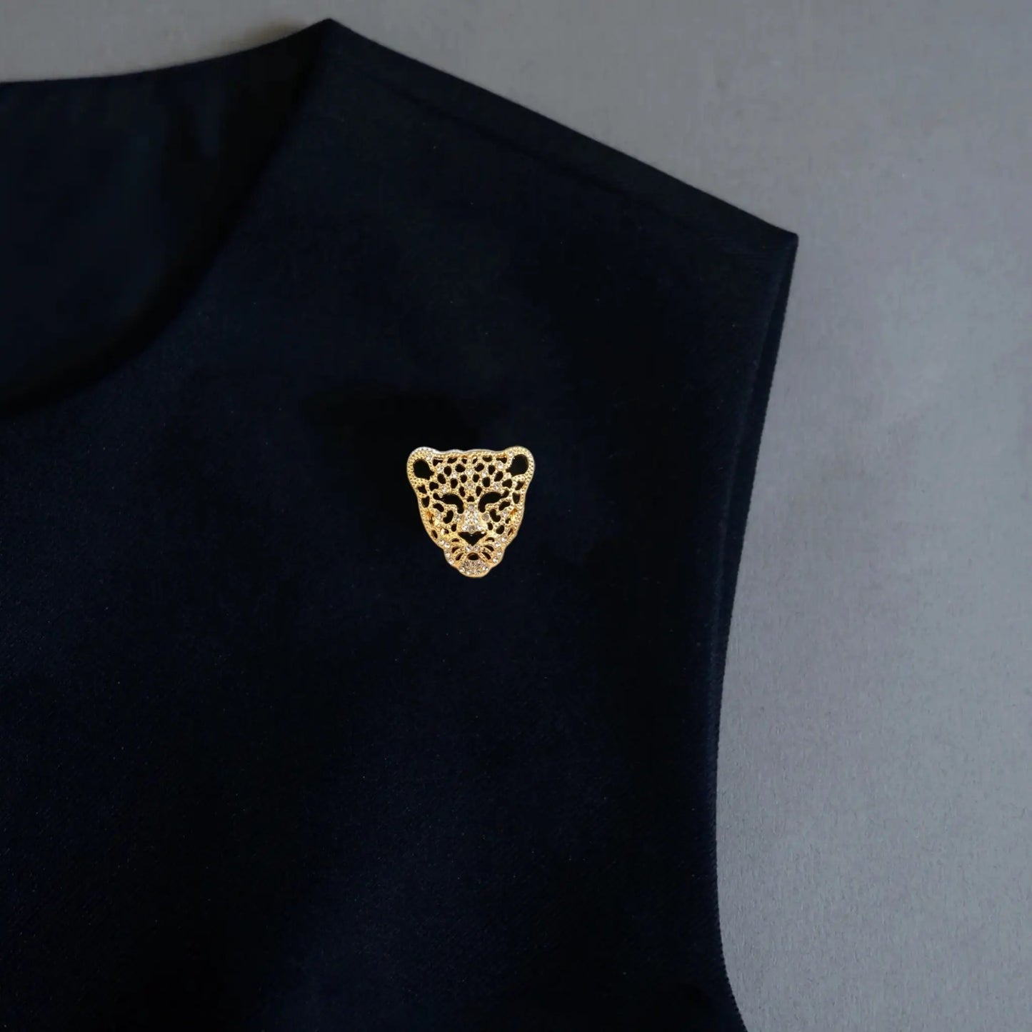 A striking styling shot featuring a 2-in-1 hollowed gold panther head accessory, utilized as a bold statement brooch on a black sleeveless top. Delicately encrusted with crystals, this fierce leopard design adds a powerful, luxurious touch to any minimalist dark outfit.