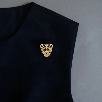 A striking styling shot featuring a 2-in-1 hollowed gold panther head accessory, utilized as a bold statement brooch on a black sleeveless top. Delicately encrusted with crystals, this fierce leopard design adds a powerful, luxurious touch to any minimalist dark outfit.