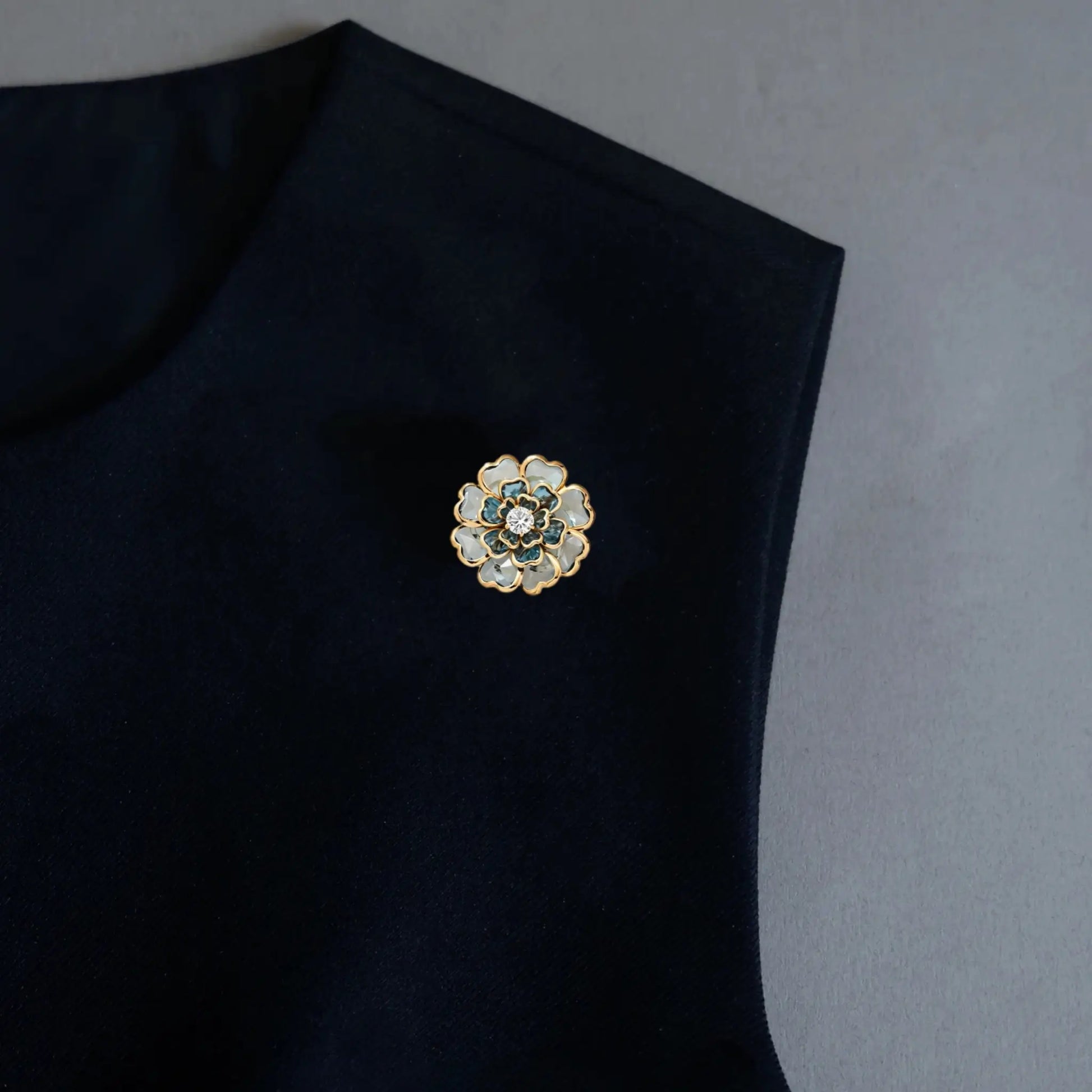 An elegant styling shot demonstrating the versatile 2-in-1 design of our floral accessory, worn here as a chic brooch pin on a black garment. Featuring light blue and white layered petals with gold edges, it adds an effortless light luxury touch to minimalist outfits.