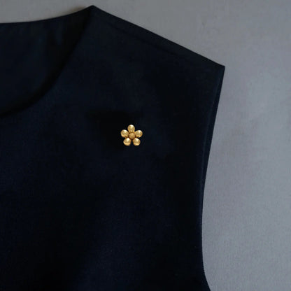 A refined styling image displaying a versatile 2-in-1 matte gold floral accessory elegantly utilized as a chic brooch on a dark top. The petite five-petal design and frosted gold finish perfectly embody the old money aesthetic for a sophisticated, minimalist wardrobe.
