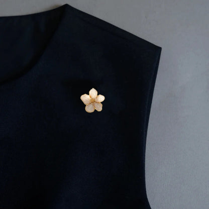 A refined minimalist styling shot demonstrating the 2-in-1 functionality of a pearlescent white floral accessory, elegantly utilized as a lapel pin on a black top. The luminous shell-like finish perfectly embodies the old money aesthetic for a sophisticated European and American look.