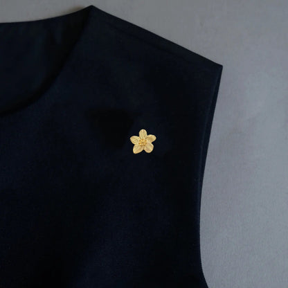 A refined minimalist styling shot featuring a 2-in-1 petite textured gold floral accessory, elegantly worn as a delicate brooch pin on a black garment. This finely crafted, light luxury piece perfectly embodies the quiet luxury aesthetic, offering a subtle yet sophisticated statement for modern wardrobes.