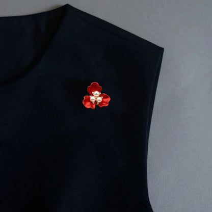 An elegant styling shot featuring a versatile 2-in-1 red enamel floral accessory worn as a chic brooch pin on a black sleeveless garment. Accented with a beautiful three-pearl center, this versatile piece adds a vibrant pop of color and light luxury to everyday outfits.