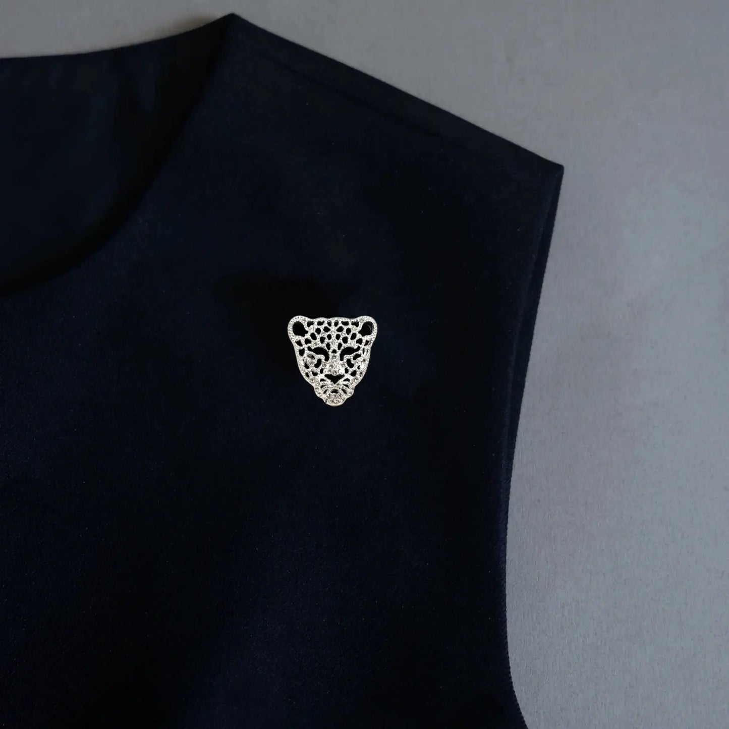 A sophisticated minimalist photo demonstrating the 2-in-1 functionality of a silver panther head accessory, styled as an elegant lapel pin on a black garment. The intricate hollowed design and sparkling crystal details offer a sleek, commanding quiet luxury statement for modern women.