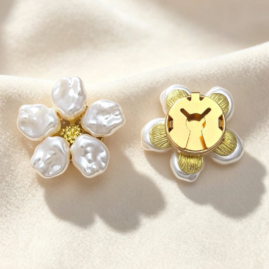 Elegant baroque pearl floral button covers with a textured gold center, resting on soft cream fabric under warm sunlight. The right piece highlights the secure closed gold backing, functioning perfectly as a light luxury faux cufflink.