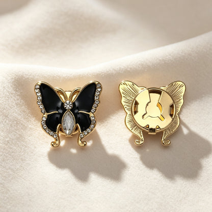 Elegant black enamel butterfly button cover featuring a marquise crystal body and rhinestone-encrusted wings. Resting on soft cream fabric, the right piece highlights the secure closed gold backing, perfect as a light luxury faux cufflink.