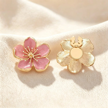Delicate blush pink enamel floral button cover featuring an intricate gold stamen center. Resting on soft cream fabric, the right piece shows the open gold clasp mechanism, designed for a seamless and elegant faux cufflink upgrade.