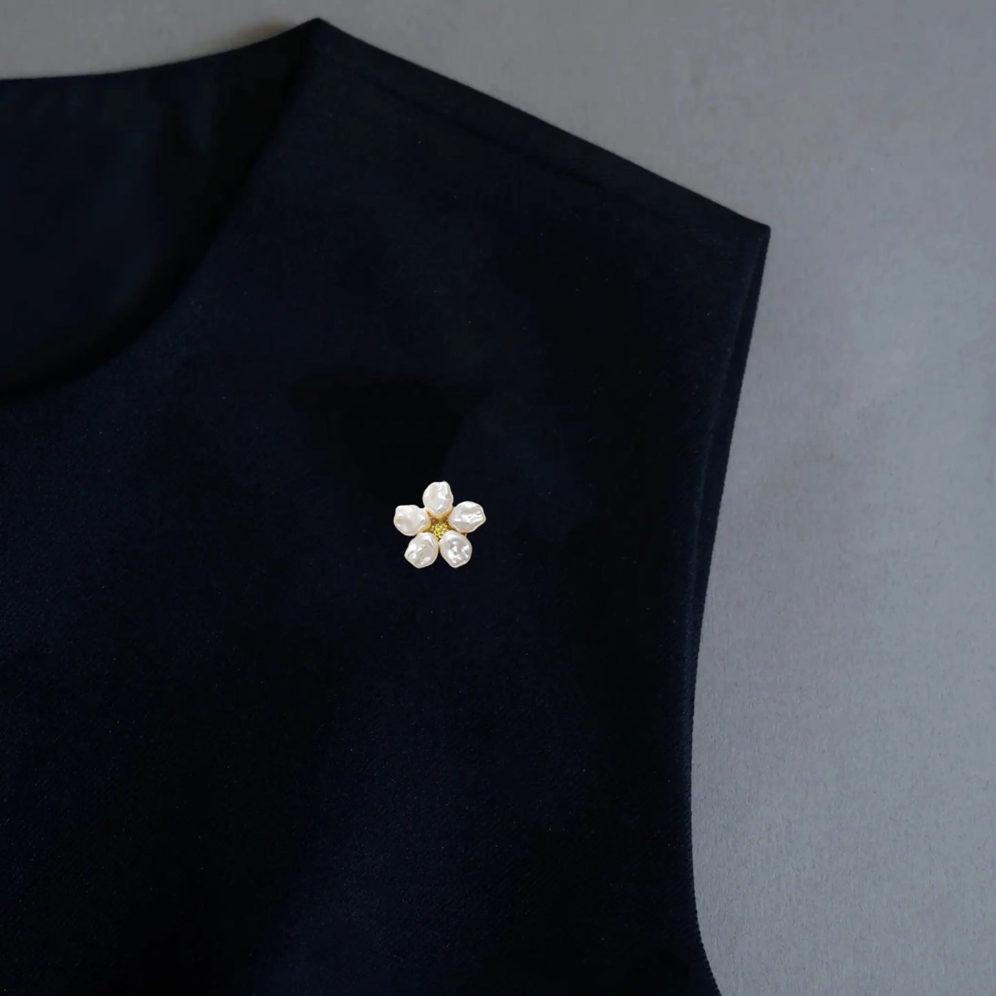 A close-up lifestyle shot of a woman elegantly styling a black silk blouse. Her double-button cuff is adorned with two realistically scaled brushed silver floral button covers, each featuring a pearl center. These delicately proportioned faux cufflinks perfectly mimic standard buttons, seamlessly adding a touch of sophisticated, everyday luxury to the modern outfit.