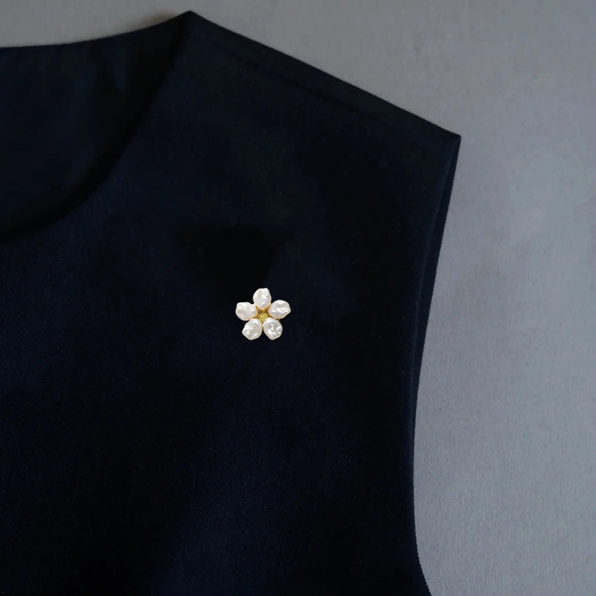 A close-up lifestyle shot of a woman elegantly styling a black silk blouse. Her double-button cuff is adorned with two realistically scaled brushed silver floral button covers, each featuring a pearl center. These delicately proportioned faux cufflinks perfectly mimic standard buttons, seamlessly adding a touch of sophisticated, everyday luxury to the modern outfit.