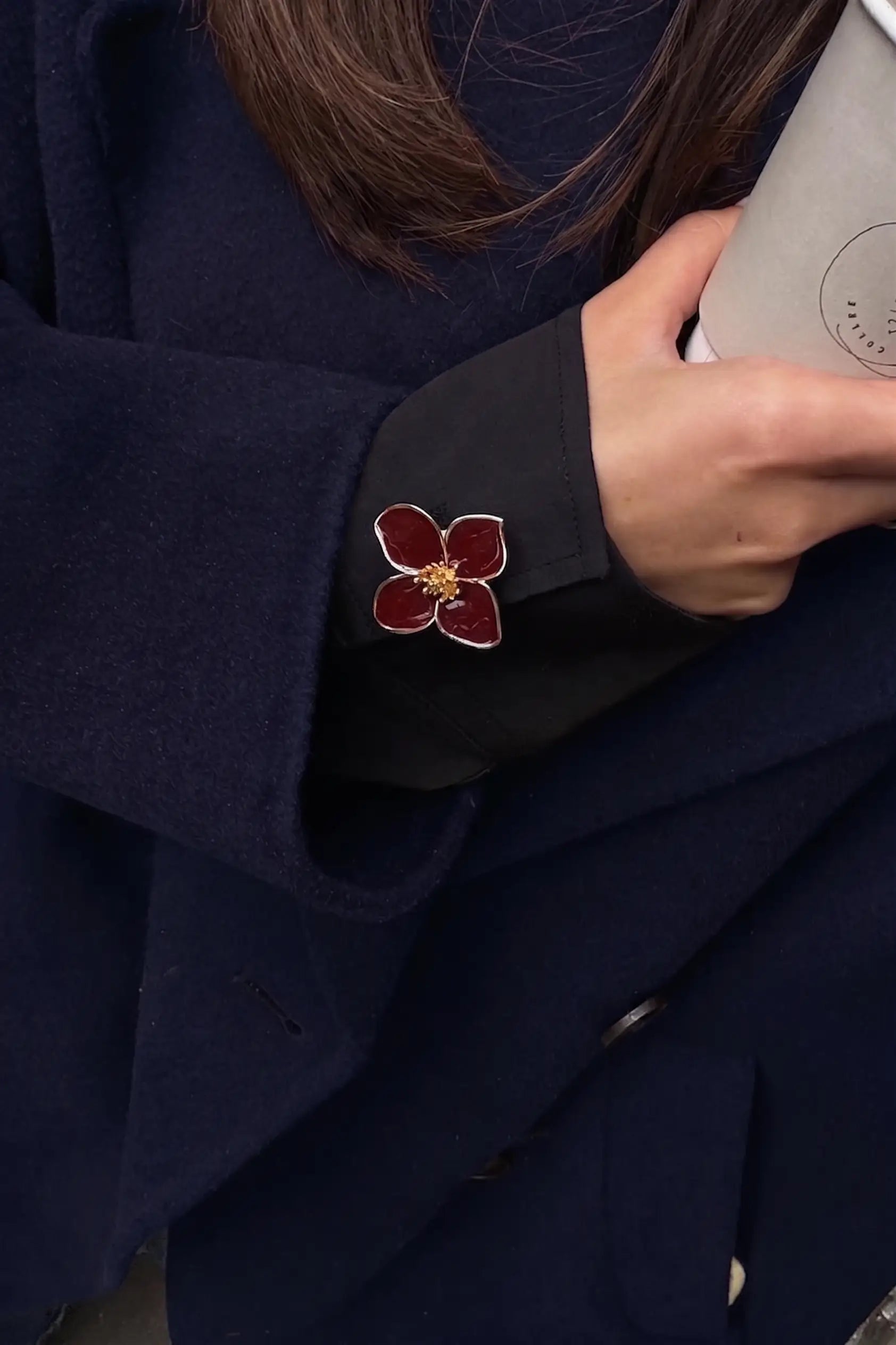 Close-up of a woman holding a coffee cup, showcasing a deep burgundy enamel four-petal floral button cover on her black cuff. Paired with a navy blue wool coat, this styling shot perfectly captures a sophisticated, dark academia aesthetic for modern winter commutes.