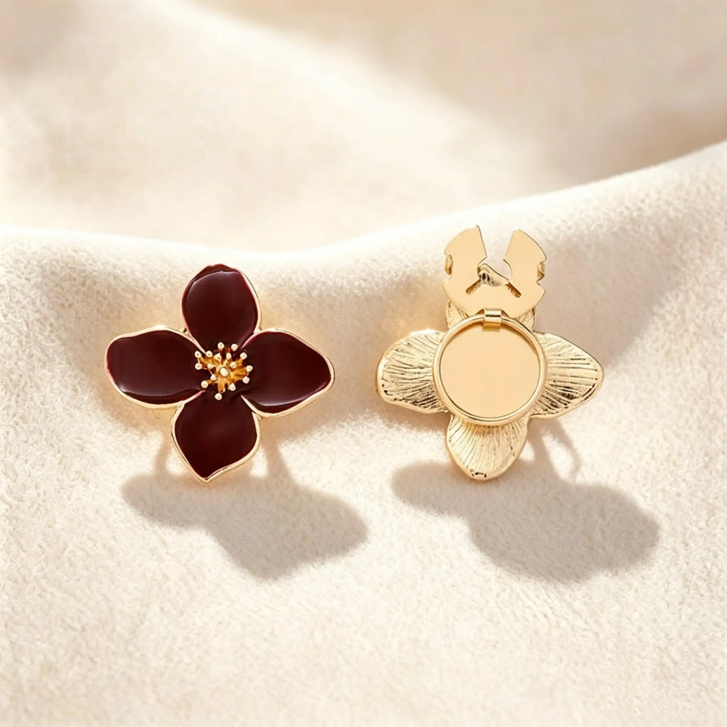 A classic burgundy wine red enamel four-petal floral button cover distinguished by its intricately textured gold stamen. Accompanied by the open gold back clip on a cream setting, it offers a sophisticated pop of color and an instant quiet luxury transformation.