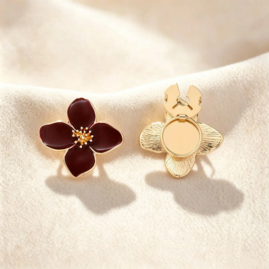 A classic burgundy wine red enamel four-petal floral button cover distinguished by its intricately textured gold stamen. Accompanied by the open gold back clip on a cream setting, it offers a sophisticated pop of color and an instant quiet luxury transformation.