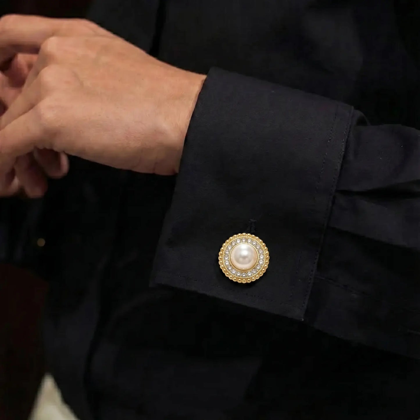 Close-up of a person adjusting their black shirt cuff, elegantly secured with a classic round pearl and rhinestone button cover. An ideal, easy-to-use cuff accessory for modern daily office wear.