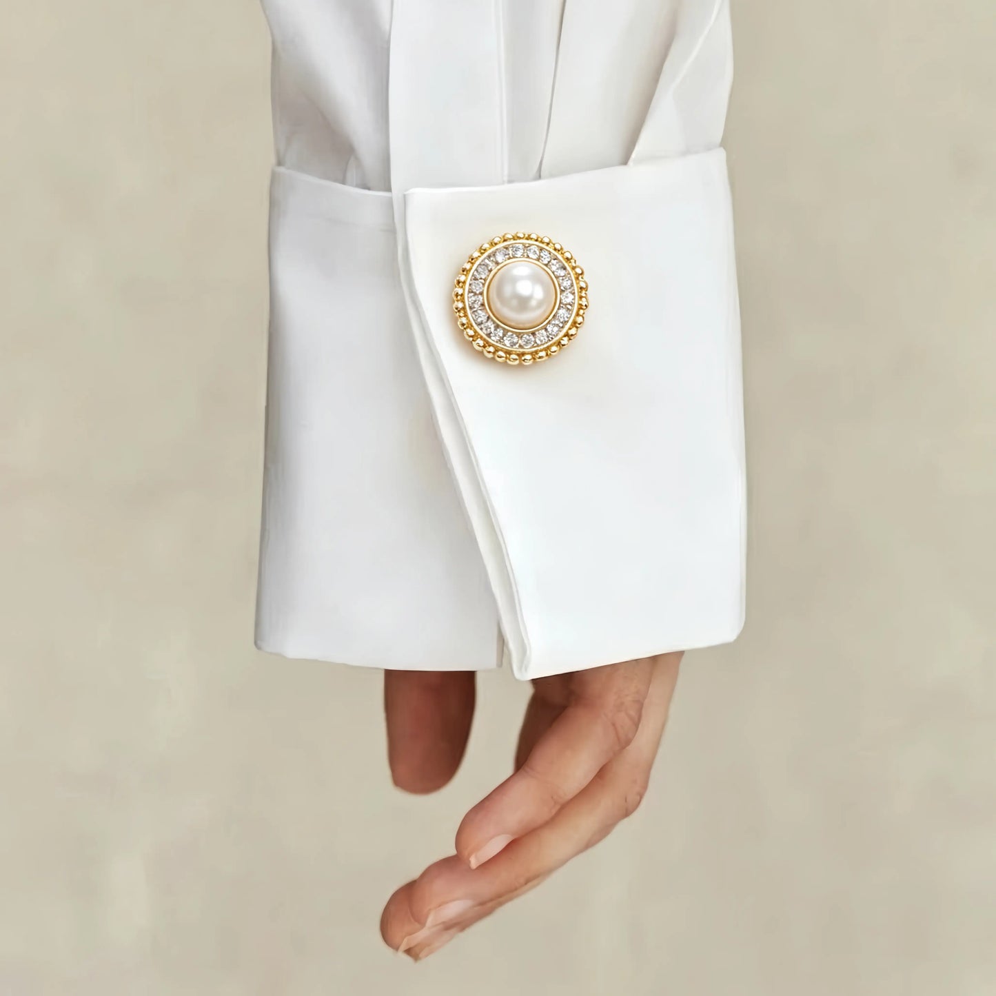 A sophisticated lifestyle shot of a classic round pearl button cover with a rhinestone halo and gold beaded edge. Elegantly styled as a faux cufflink on a crisp white shirt cuff, demonstrating an effortless light luxury upgrade for everyday office wear.