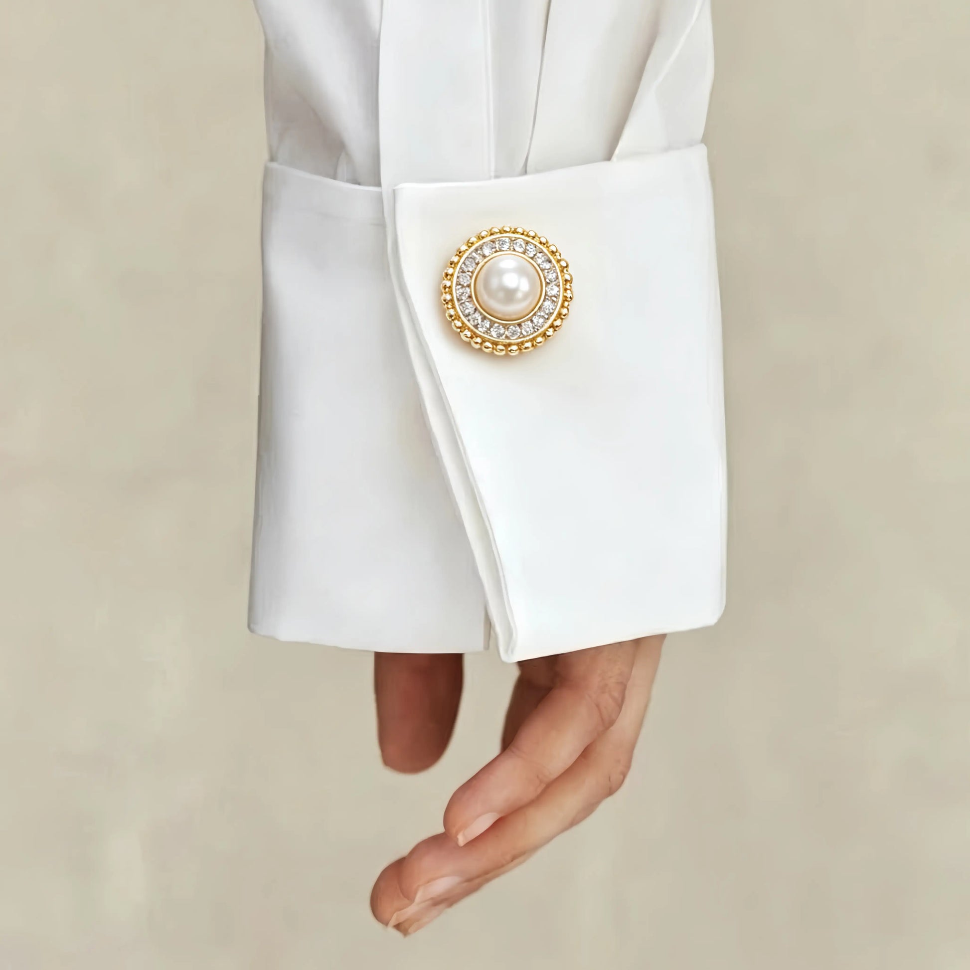 A sophisticated lifestyle shot of a classic round pearl button cover with a rhinestone halo and gold beaded edge. Elegantly styled as a faux cufflink on a crisp white shirt cuff, demonstrating an effortless light luxury upgrade for everyday office wear.