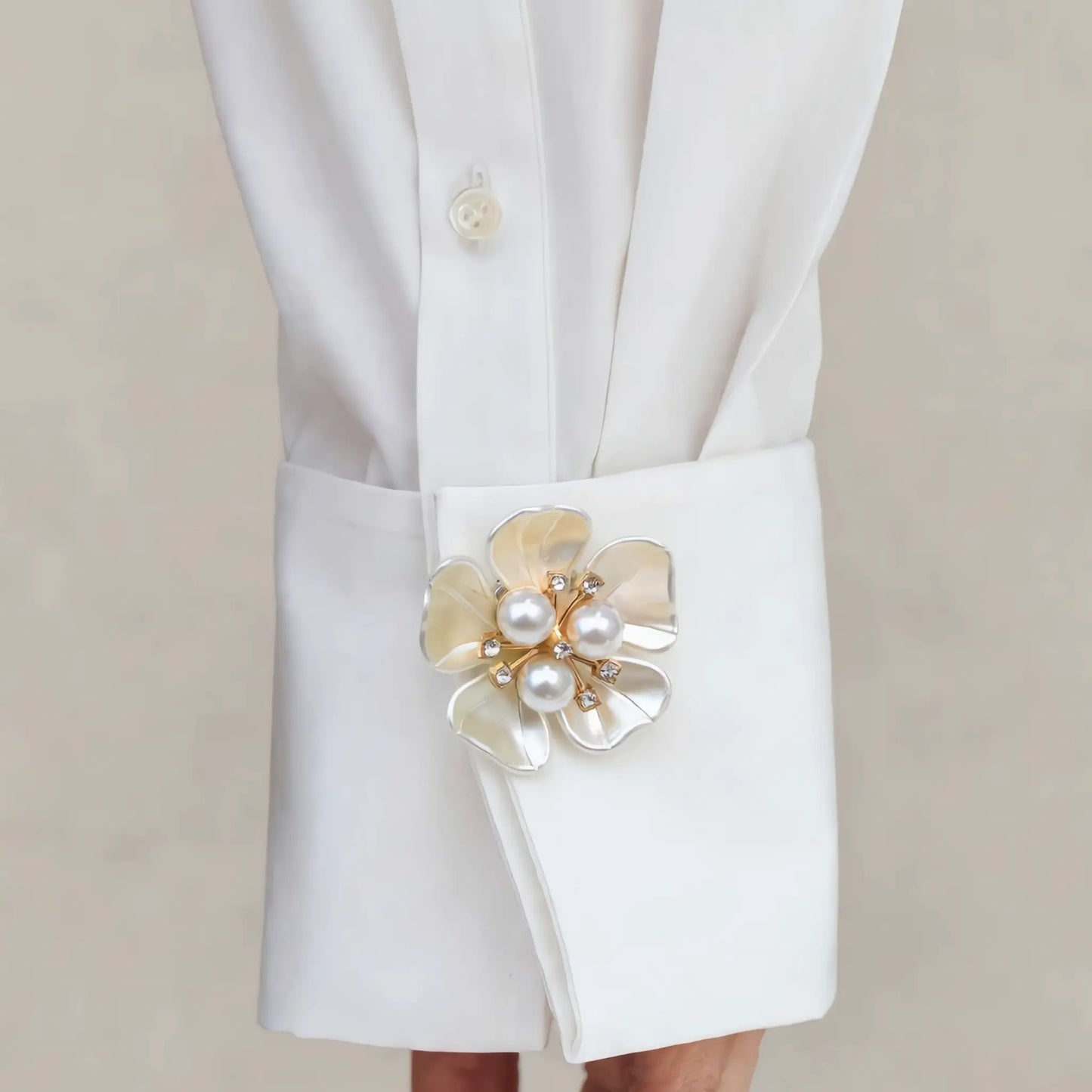 A lifestyle styling shot of a refined creamy white floral button cover with a three-pearl center, elegantly secured on a crisp white shirt cuff. This perfectly proportioned light luxury faux cufflink offers a seamless tone-on-tone aesthetic, avoiding the look of a heavy brooch for a realistic, everyday French-style cuff upgrade.