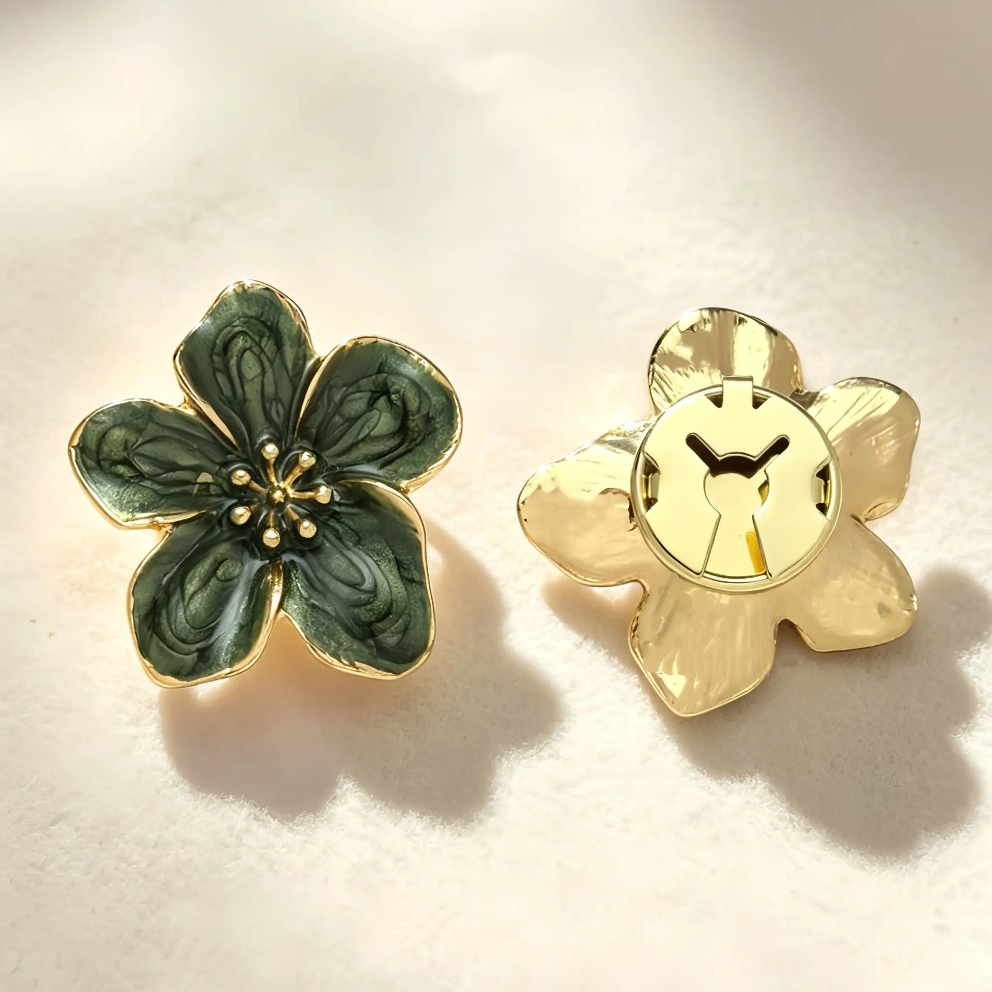 A pair of deep green vintage enamel floral button covers resting on soft fabric with natural shadow play. The right side shows the closed gold clip mechanism, ensuring a secure fit when styled as a luxurious French-cuff alternative.