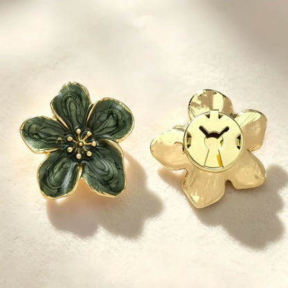 A pair of deep green vintage enamel floral button covers resting on soft fabric with natural shadow play. The right side shows the closed gold clip mechanism, ensuring a secure fit when styled as a luxurious French-cuff alternative.