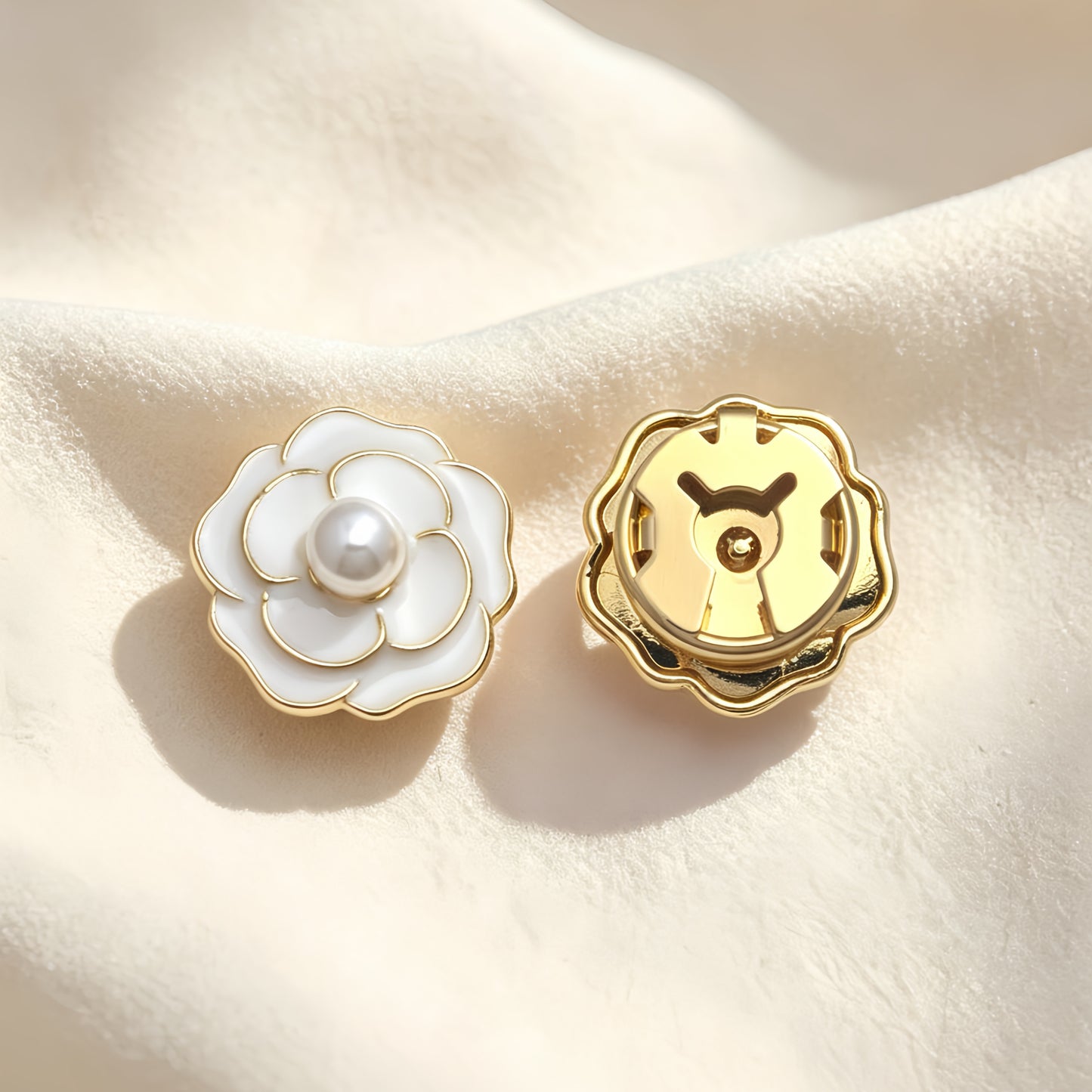 A pair of beautiful white enamel camellia button covers with a pearl core. The image emphasizes the closed gold backing, ensuring a seamless and secure fit when worn as an elegant faux cufflink.