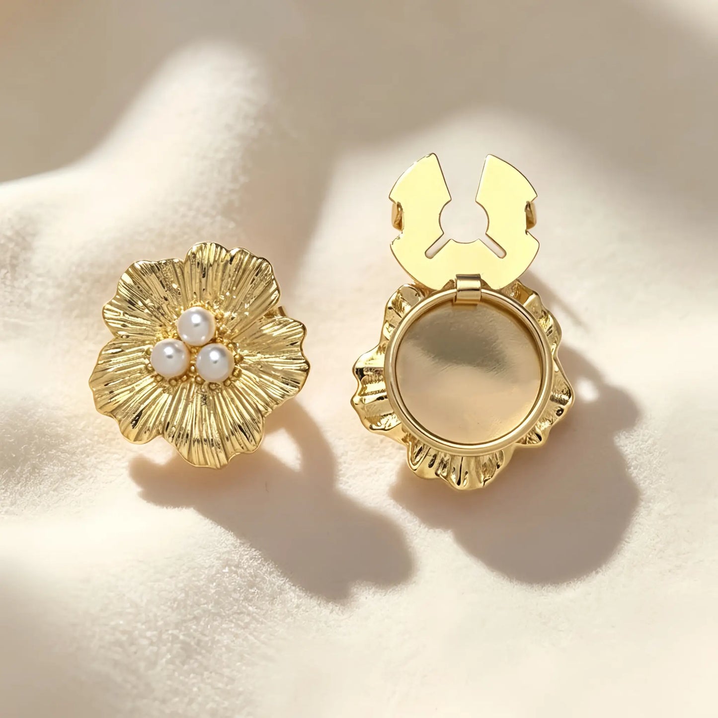 Beautiful textured gold floral button cover centered with three classic white pearls. Shown with the gold attachment clip fully open on soft cream fabric, demonstrating an effortless and elegant shirt cuff upgrade.