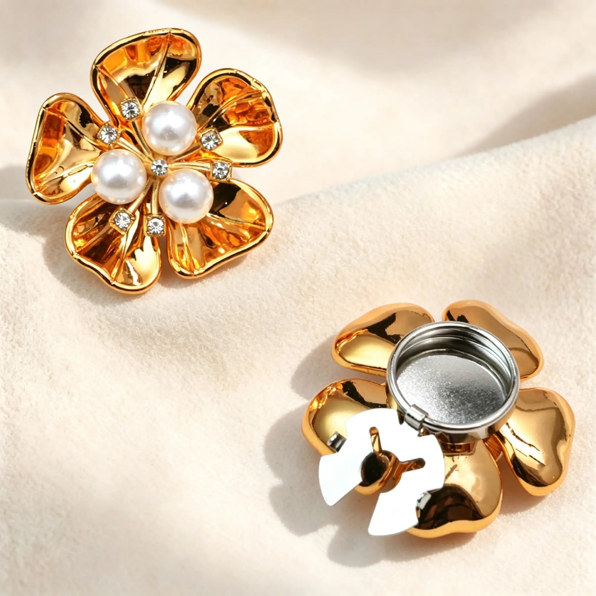 High-shine glossy gold floral button cover centered with three white pearls and sparkling rhinestones. Includes a detailed view of the gold open clasp back, designed to securely fit over standard shirt cuffs.