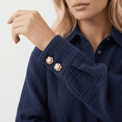 Close-up of a woman's wrist showing a modern textured cotton shirt with a double-button cuff, elegantly secured by two delicately scaled gold and pearl floral button covers. A refined, perfectly proportioned everyday cuff accessory that mimics the size of standard buttons.