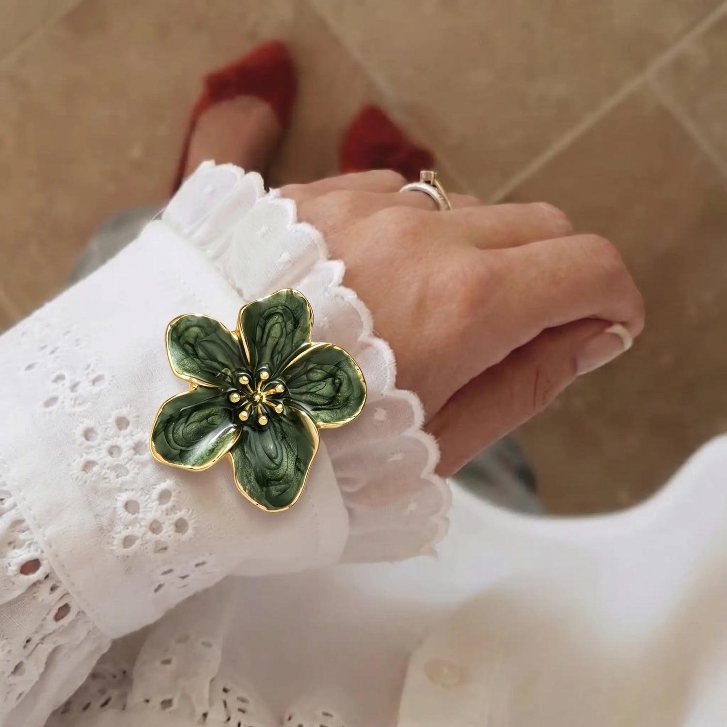 A lifestyle shot of a woman wearing a white lace-trimmed casual blouse, styled with a vintage green enamel floral button cover on the cuff. A perfect faux cufflink for an effortless everyday chic look.