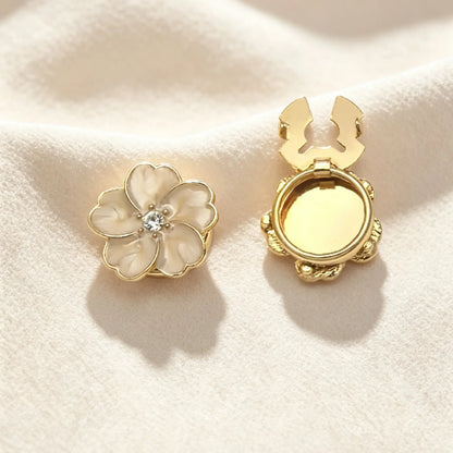 Classic ivory white enamel five-petal floral button cover with gold accents and a sparkling rhinestone. Displayed with the gold clasp fully open, serving as a versatile and elegant shirt accessory.