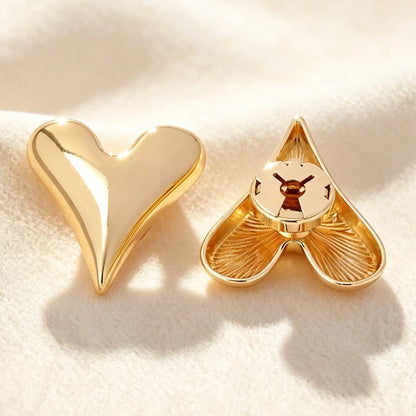Close-up of a smooth gold heart faux cufflink on a textured cream background. The image highlights the secure closed back, ensuring a seamless, zero-bulk fit against the cuff for everyday office wear.