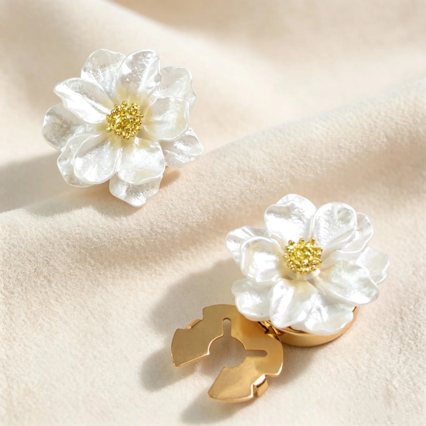 A pair of pearl white shimmering floral button covers resting on soft velvet. The image highlights both the intricate gold flower center and the secure closed gold back mechanism for effortless shirt styling.