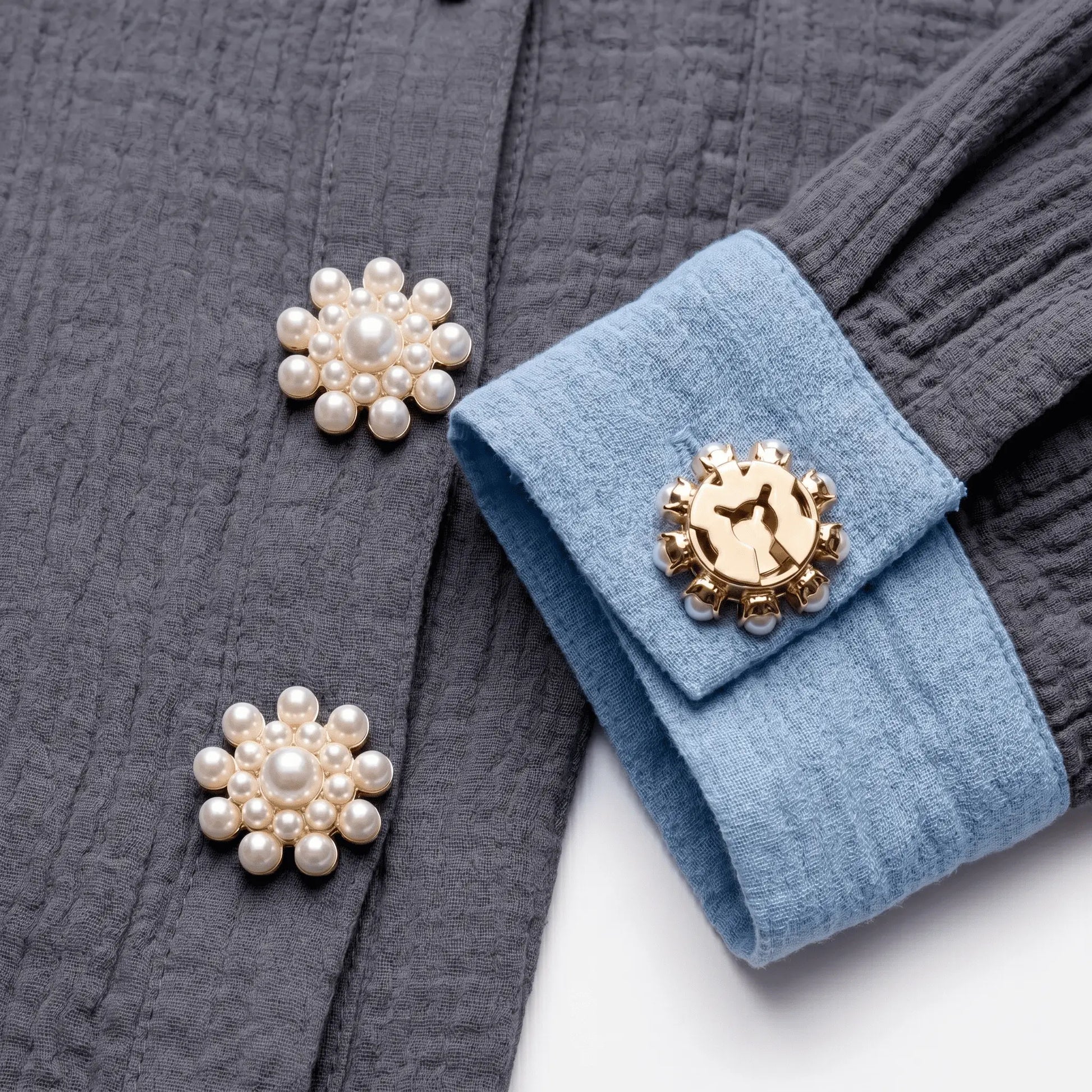 A creative flat lay styling shot featuring a modern textured grey cotton shirt with a light blue contrast cuff. Two realistically scaled pearl cluster sunflower button covers adorn the front placket, while a third is shown from the back, seamlessly securing the blue cuff with its gold clip. A versatile, light luxury faux cufflink that perfectly replaces standard buttons for everyday fashion.