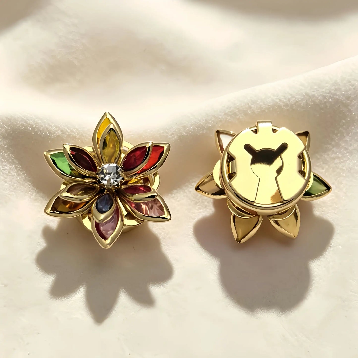 Detailed view of a light luxury rainbow-colored lotus button cover resting on soft cream fabric. The right piece highlights the secure closed gold backing, demonstrating its flawless use as an elegant French-style cuff accessory.