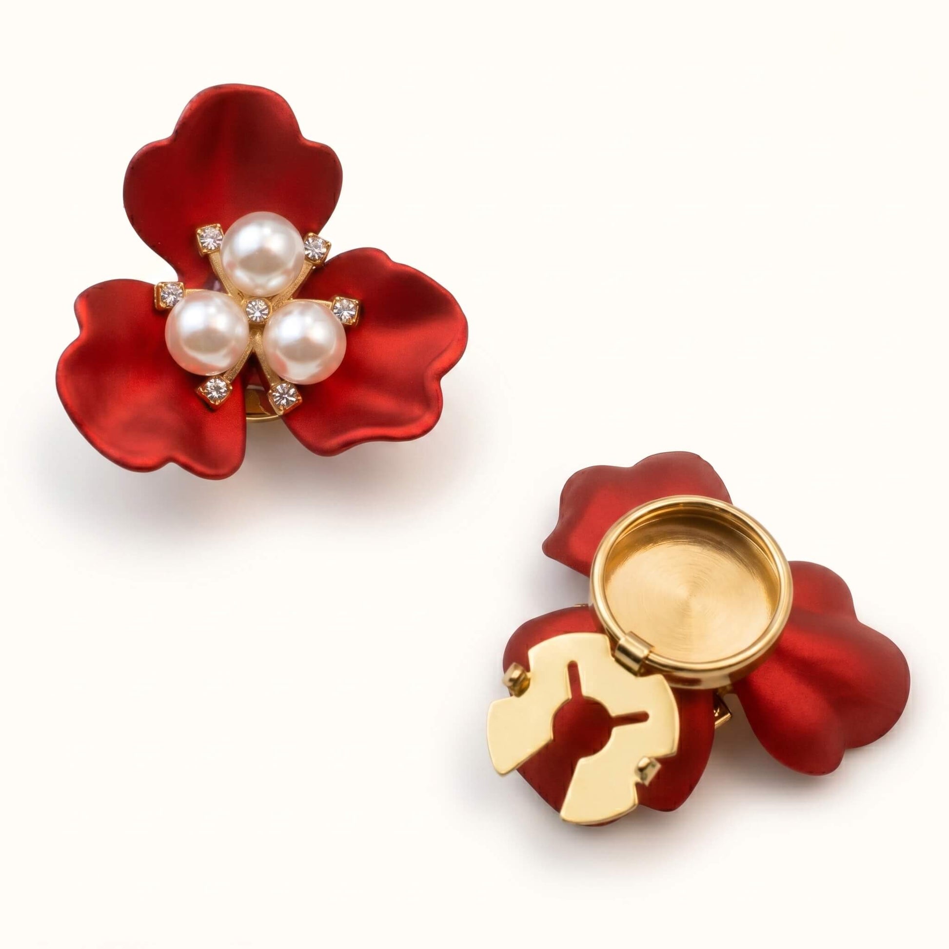 A bold red flower-shaped button cover with delicate pearl accents and a secure gold hinge, perfect for adding a sophisticated touch to basic button-down shirts.