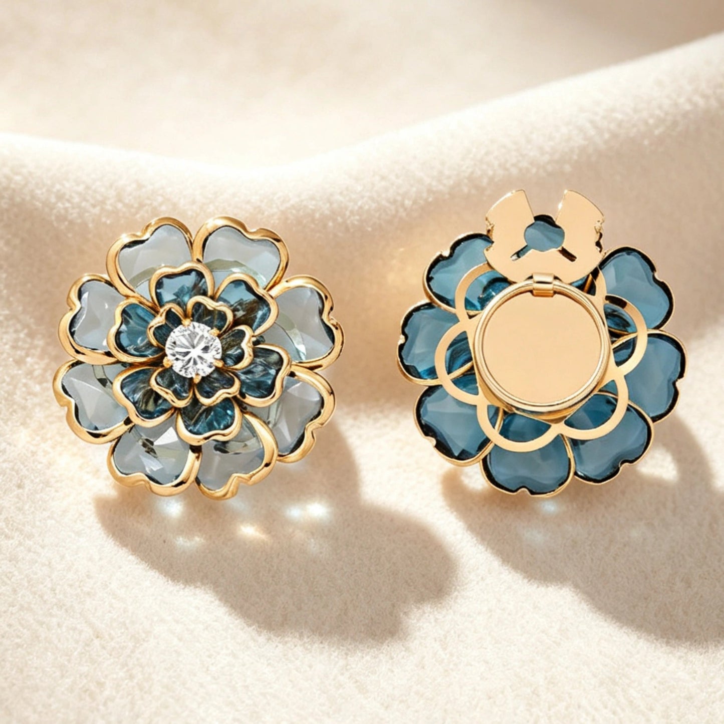 Elegant sapphire blue layered crystal floral button cover with gold edges and a rhinestone center. Shown with the open gold clip mechanism on soft fabric, perfect as a light luxury cuff accessory.