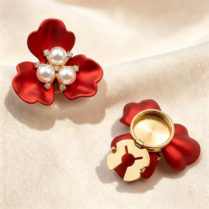 Vibrant satin red three-petal floral button cover centered with three white pearls and sparkling rhinestones. The right piece highlights the open gold attachment clip for effortless French-style cuff styling under warm sunlight.