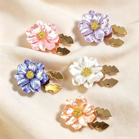 A beautifully arranged collection of five shimmering pearlescent floral button covers on warm velvet fabric. Showcasing color options in blush pink, lavender, deep purple, pearl white, and champagne peach. An ideal French-style cuff accessory gift set.