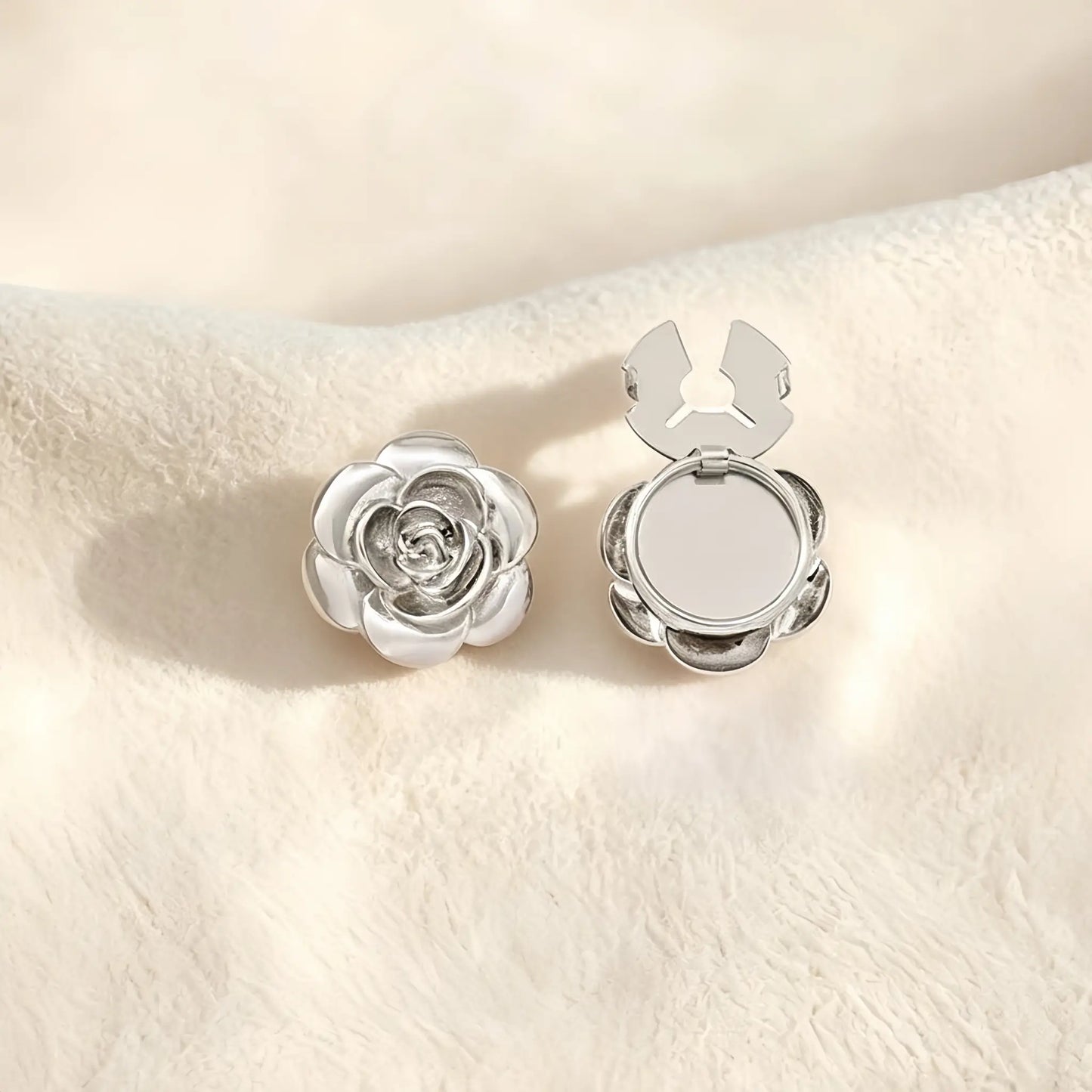 A sophisticated silver 3D rose button cover with delicate layered petals resting on a soft cream surface. The open silver clasp demonstrates the effortless functionality of this elegant faux cufflink accessory.
