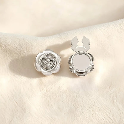 A sophisticated silver 3D rose button cover with delicate layered petals resting on a soft cream surface. The open silver clasp demonstrates the effortless functionality of this elegant faux cufflink accessory.
