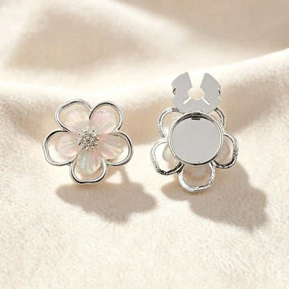 An ethereal silver five-petal floral button cover featuring translucent pearlescent inlay and a sparkling crystal center. Set against a soft cream background, the open clasp demonstrates the effortless, no-sew transformation into a chic faux cufflink.