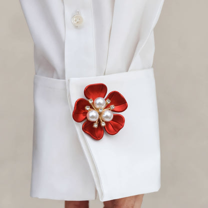A close-up lifestyle shot of a crisp white shirt sleeve, instantly elevated by a statement red floral button cover with a three-pearl center. A vibrant faux cufflink perfect for adding a pop of color and a touch of everyday fashion to basic outfits.