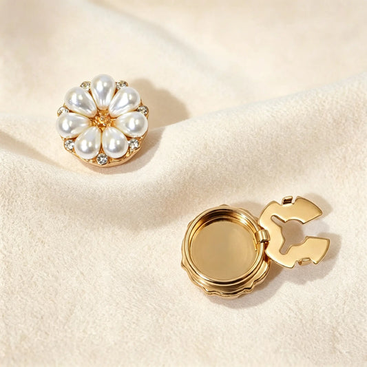 Elegant vintage-style floral button cover featuring teardrop pearl petals, sparkling rhinestone accents, and a gold center. Resting on soft cream fabric under warm sunlight. The right piece highlights the secure closed gold back clasp, functioning perfectly as a light luxury no-sew faux cufflink.