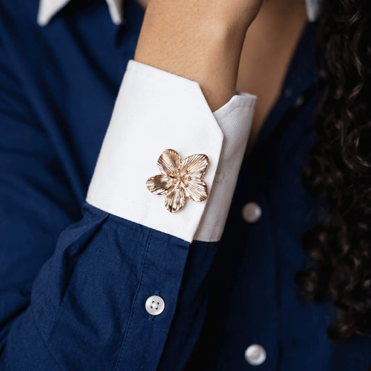 A lifestyle shot of a woman wearing a modern navy blue cotton shirt with contrast white cuffs, elegantly styled with a realistically proportioned textured gold floral button cover. A perfect light luxury faux cufflink for everyday quiet luxury fashion.