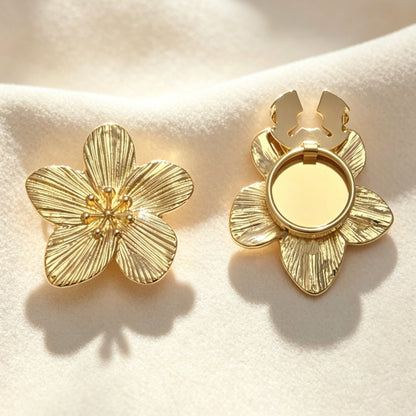 A pair of light luxury textured gold floral button covers resting on soft cream fabric under warm sunlight. The left piece shows the intricate engraved petals, while the right displays the open gold hinge mechanism, perfect for a no-sew French cuff upgrade.