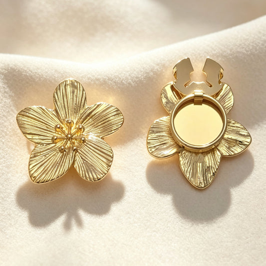 A pair of light luxury textured gold floral button covers resting on soft cream fabric under warm sunlight. The left piece shows the intricate engraved petals, while the right displays the open gold hinge mechanism, perfect for a no-sew French cuff upgrade.