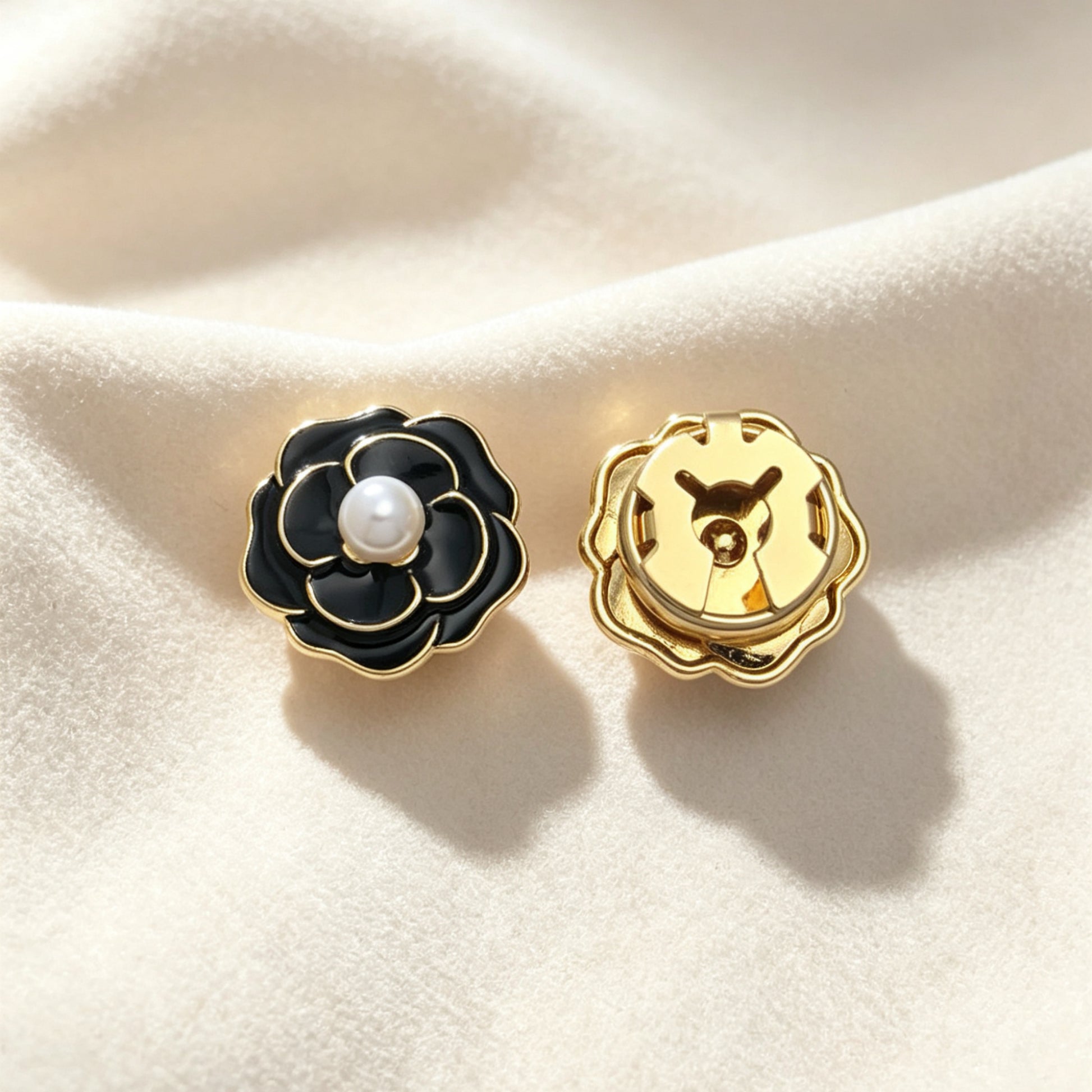 Detailed view of a light luxury black camellia button cover resting on soft cream fabric. The image highlights the secure closed gold clip back, functioning flawlessly as a sophisticated vintage cuff accessory.